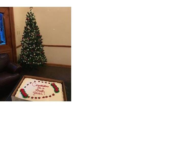 A sheet cake is in the front with a decorated Christmas tree in the background